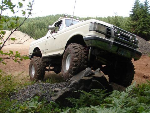 1996 Ford Bronco - Modified Ford pickup truck navigating a rocky trail with dense forest in the background.