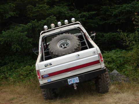 1996 Ford Bronco - Modified Ford Bronco parked on an incline with trees in the background. Spare tire is visible in the bed.