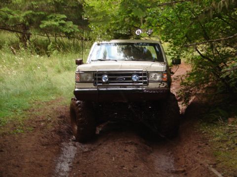 1996 Ford Bronco - A lifted Ford Bronco navigates a muddy off-road path through a wooded area.