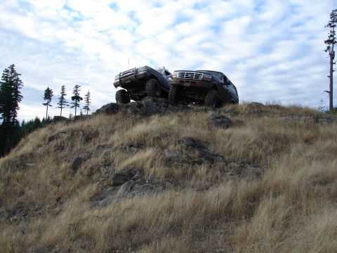 1996 Ford Bronco - Two 1996 Ford Broncos navigate a challenging rocky incline, their off-road capabilities under a dynamic sky.
