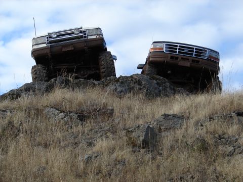 1996 Ford Bronco - Two SUVs navigate a challenging rocky incline under a cloudy sky.