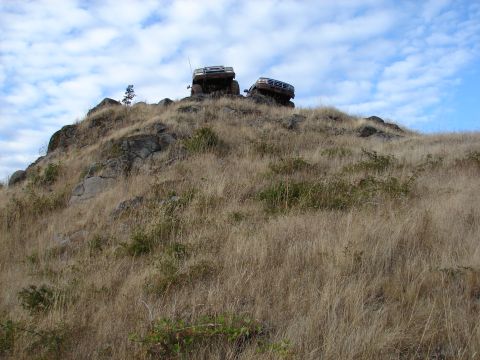 1996 Ford Bronco - Two SUVs are positioned on a rocky, dry hillside with sparse vegetation under a partly cloudy sky.