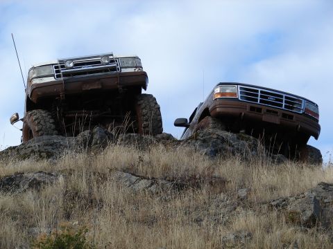 1996 Ford Bronco - Two trucks, a brown Ford Explorer and a white vehicle, navigate a rocky incline under a cloudy sky.