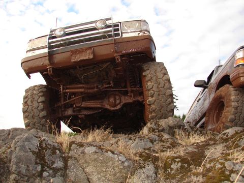 1996 Ford Bronco - Two muddy trucks navigating a rocky off-road trail.