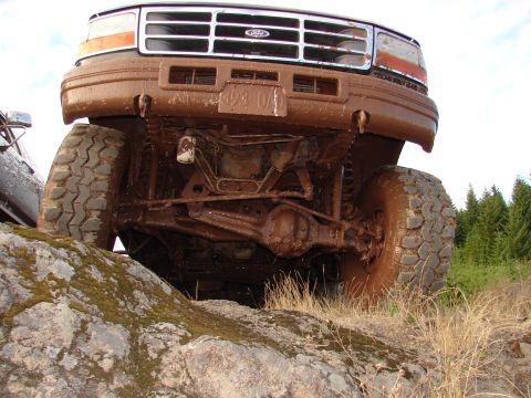 1996 Ford Bronco - This heavily mud-caked truck is navigating rough terrain, with its front grille and tires clearly visible.