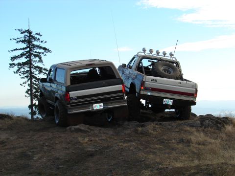 1996 Ford Bronco - Two lifted Ford Broncos navigate a , rocky terrain under a clear blue sky.