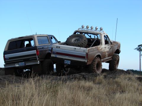 1996 Ford Bronco - Two Ford Broncos tackle a rocky, off-road trail under a clear blue sky.