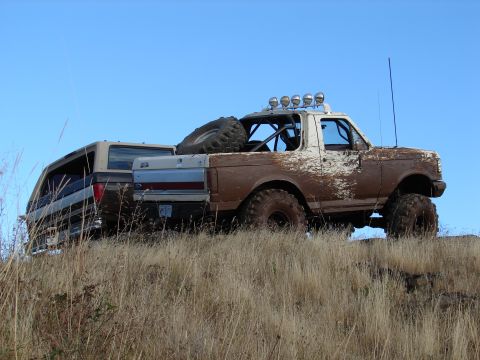1996 Ford Bronco - Two off-road SUVs are parked on a dry, grassy hill with a clear blue sky above.