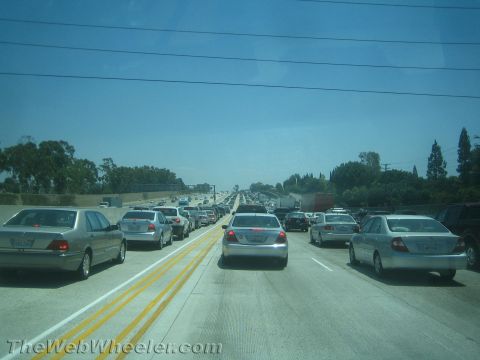 1990 Ford Bronco - Bumper-to-bumper freeway traffic with sedans and a semi-truck stopped across multiple lanes under a clear blue sky.