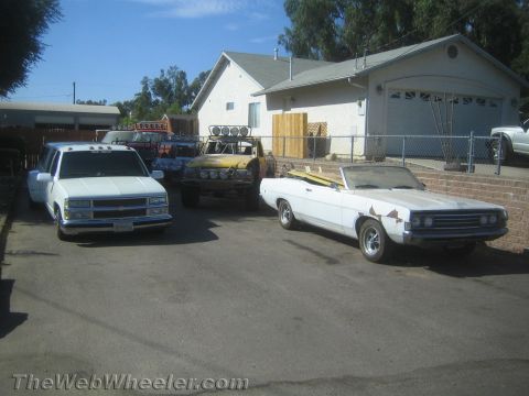 1990 Ford Bronco - white pickup, a yellow off-road truck and a weathered white convertible parked in a residential driveway.