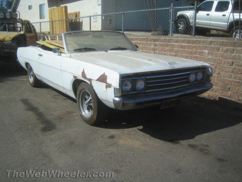 1990 Ford Bronco - weathered white convertible with dual stacked headlights and peeling body paint parked beside a brick wall.