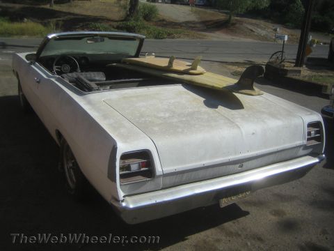 1990 Ford Bronco - Rear of a weathered white convertible, top down with a surfboard inside, showing chrome bumper and twin taillights.