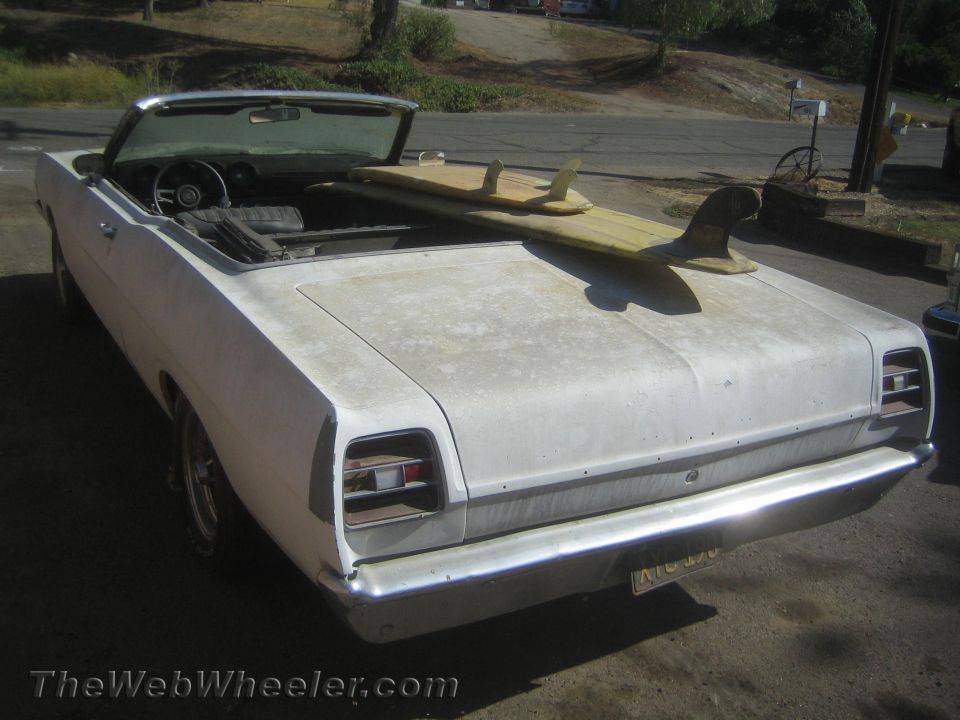 Rear of a white vintage convertible with surfboard, top down, chrome bumper