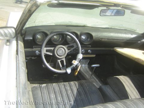 1990 Ford Bronco - Interior of a vintage convertible showing a three-spoke steering wheel, round dash gauges and worn black seats.