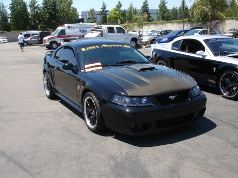 1993 Ford Taurus - A black Ford Mustang with a carbon fiber hood and a yellow banner on the windshield is parked in a lot next to another Mustang.