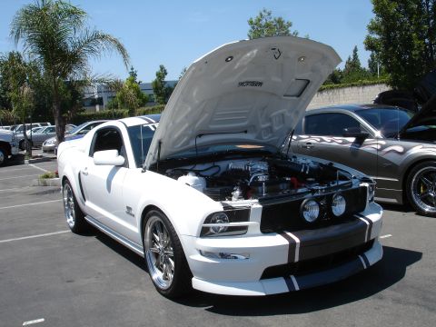 1993 Ford Taurus - A white Ford Mustang is parked with its hood open, revealing the engine, alongside another car with flame graphics.