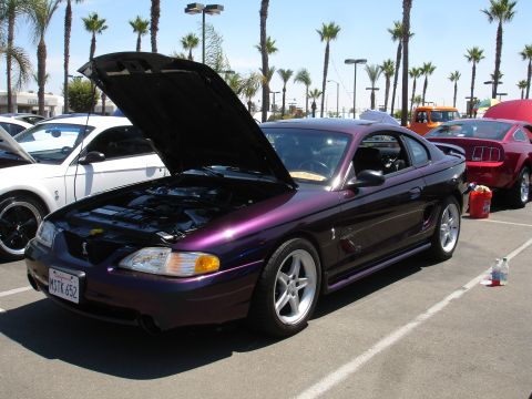 1993 Ford Taurus - A purple Ford Mustang is parked at an outdoor event with its hood open, showing the engine bay.