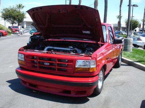 1993 Ford Taurus - A red 1995 Ford F-150 pickup truck is parked with its hood open, revealing the engine bay.