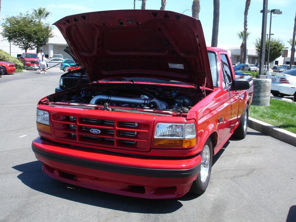 Red 1995 Ford F-150 pickup truck, front 3/4 view, hood open showing engine, parked outdoors