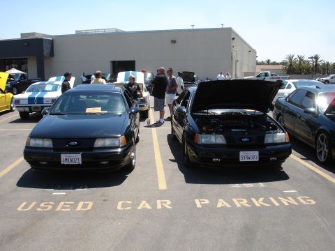 1993 Ford Taurus - Two black Ford sedans are parked in a lot, with one showing its engine.