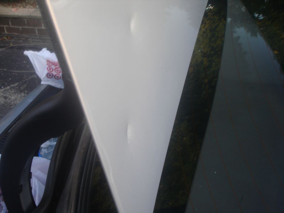 Close-up of dents on a white car body panel near roof and door frame