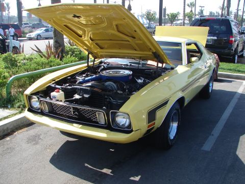 1992 Ford Taurus - A yellow classic car with its hood open, parked in a lot with other vehicles.