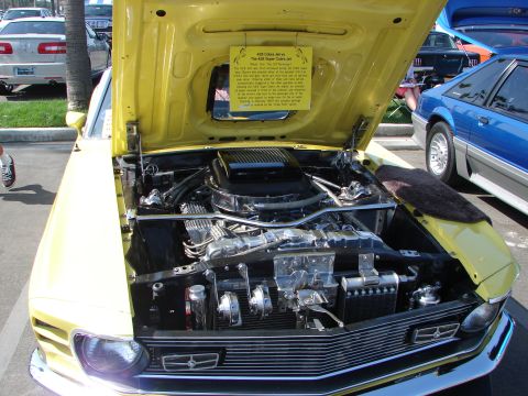 1992 Ford Taurus - A yellow 1969 Ford Mustang Mach 1 is displayed with its hood open, revealing the engine and a descriptive sign.