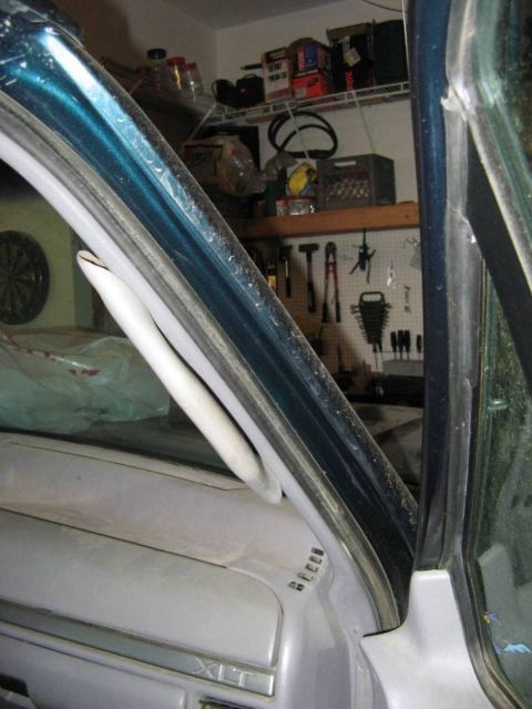 1995 Ford Bronco - Interior view up the passenger A-pillar of a teal-blue Ford with the windshield removed and the gray A-pillar trim and dash-top pad pulled…