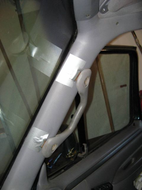 1995 Ford Bronco - Interior view of a gray A-pillar and grab handle in a truck cab, with strips of masking tape applied above and below the handle's mounting…