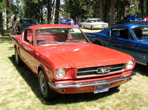 1965 Ford Mustang - A red 1965 Ford Mustang coupe is parked on grass at an outdoor car show.