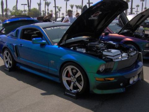 1991 Ford Taurus - A modified Ford Mustang GT displays its supercharged engine under an open hood, parked next to another custom car.
