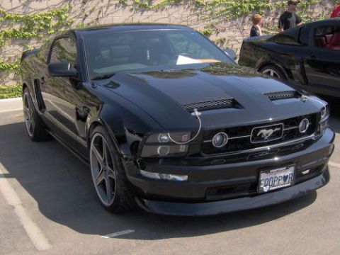 1991 Ford Taurus - This black Ford Mustang has a distinctive grille and hood scoops, with another vehicle visible behind it.