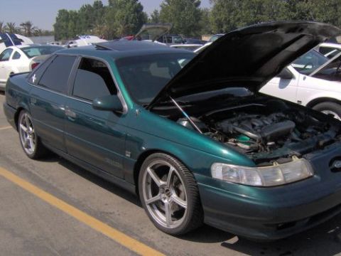 1991 Ford Taurus - Green 1991 Ford Taurus with hood open, parked outdoors with other vehicles around.