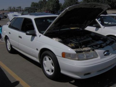 1991 Ford Taurus - A white 1991 Ford Taurus is parked with its hood open, revealing the engine bay.