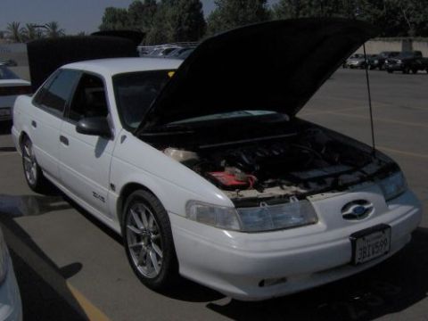 1991 Ford Taurus - A white 1991 Ford Taurus sedan is parked with its hood open, revealing the engine compartment.