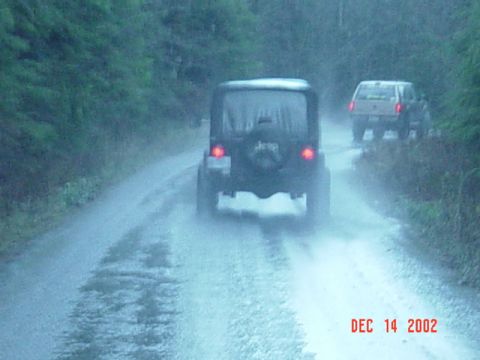 1989 Ford Bronco - Two SUVs navigate a muddy road during a downpour, as indicated by the date stamp of December 14, 2002.