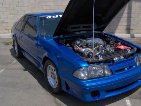 1991 Ford Taurus - This blue Ford Mustang has its hood open, revealing the engine bay and a sticker on the windshield.