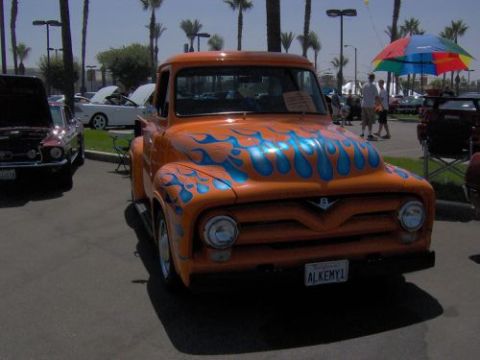 1991 Ford Taurus - An orange 1956 Ford F-100 pickup truck with blue flame graphics is parked outdoors.
