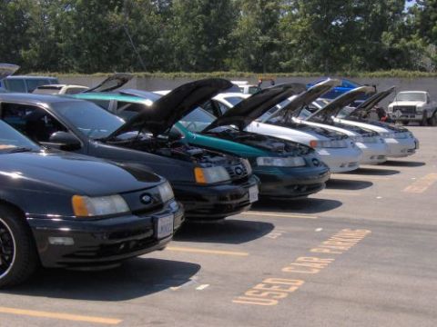 1991 Ford Taurus - A row of 1991 Ford Taurus vehicles are parked with their hoods open, suggesting a car meet or show.