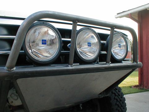 1996 Ford Bronco - The front grille of a Ford Bronco is visible behind a custom brush guard fitted with three large, round auxiliary lights.
