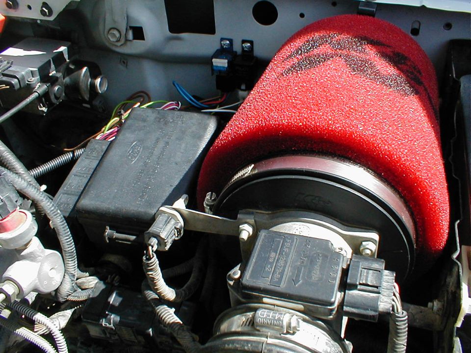 Engine bay with red cone air filter and black fuse box with Ford logo