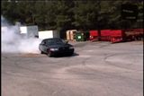 2001 Ford Crown Victoria - A black sedan drifts in a lot, creating a cloud of smoke from its tires.