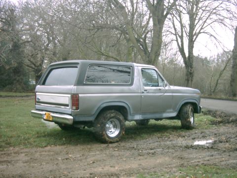 1982 Ford Bronco - This 1982 Ford Bronco is seen from the rear 3/4 angle, parked on a muddy, grassy area with trees in the background.