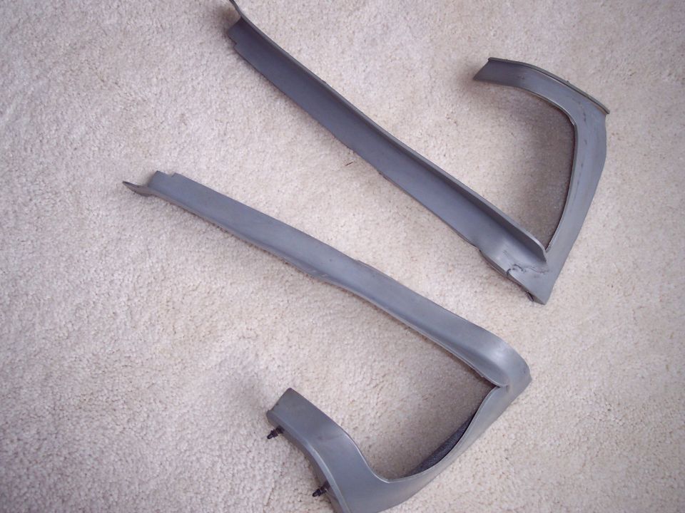 Two grey A-pillar trim mouldings on carpet showing hollow backs and black push-in clips
