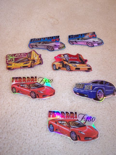 1968 Chrysler Town & Country - A variety of car stickers different sports car models are displayed on a carpeted surface.