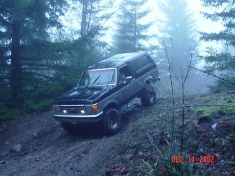 1989 Ford Bronco - 1989 Ford Bronco navigates a challenging off-road trail in a foggy, wooded area.