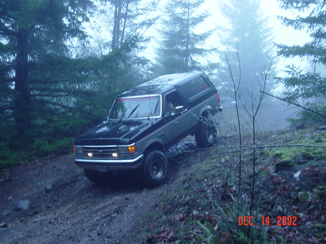 1989 Ford Bronco driving up a muddy, wooded hill