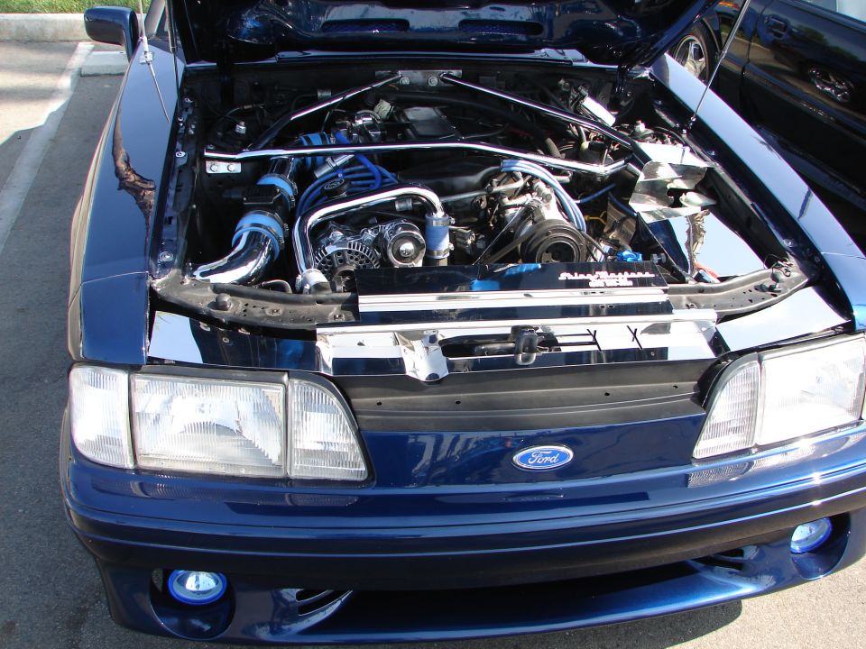 Blue Ford Mustang with hood open showing engine, chrome accents, and blue hoses