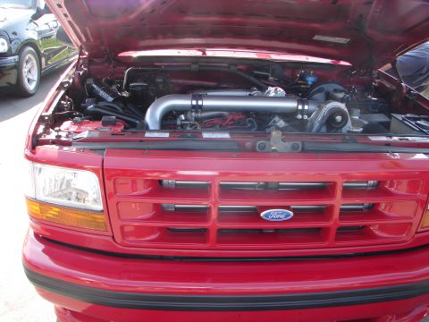 1992 Ford Taurus - Front view of a red Ford truck's engine bay and grille. A black car is parked nearby.