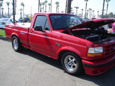 1992 Ford Taurus - A red pickup truck is parked with its hood open, revealing the engine compartment. Other vehicles and palm trees are visible in the backgro…